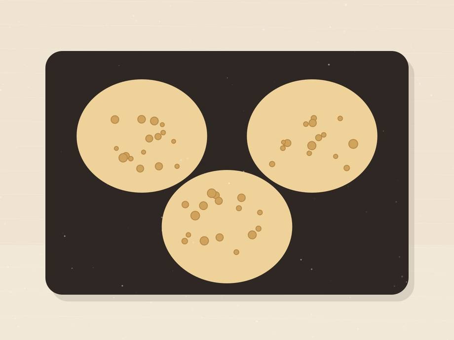 Illustrated griddle with three pancakes, their surfaces covered in open bubbles